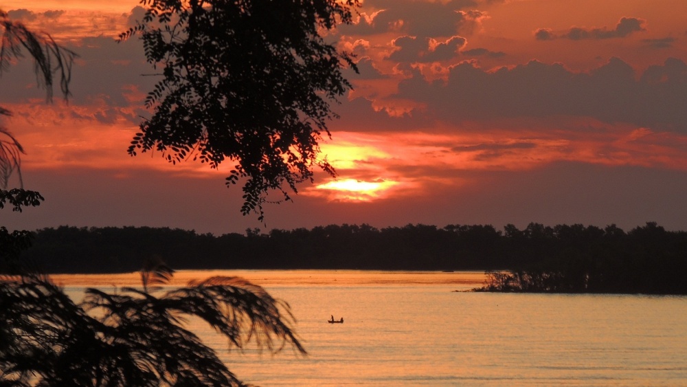 "Atardecer, sol, nubes, ro y canoa" de Sebastin Snchez