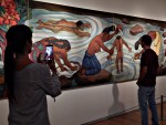 La que saca foto al que mira el mural de Rivera